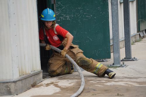 Girl in firefighting gear guiding a fire hose into a door opening