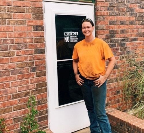 Girl in orange shirt standing by a door.