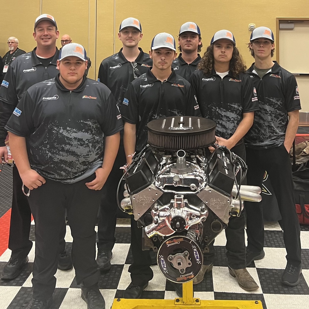 Automotive students standing behind an engine