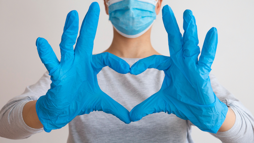 Photo of medical person holding up blue gloved hands in heart pattern