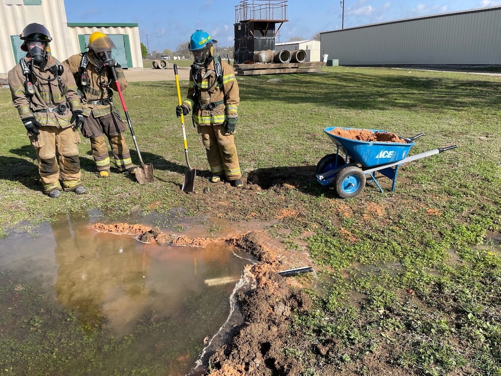 Students in fire gear standing with shovel next to simulated hazard site