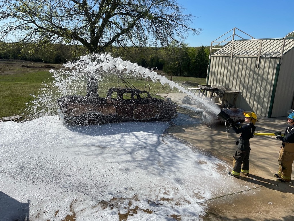 Fire student spraying foam from a hose on the ground